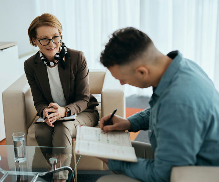 a man writing on a notebook while talking to his therapist