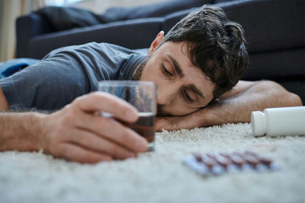 a man sleeping on carpet while holding an alcohol and benzos besides him